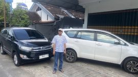 Foto: Koordinator AMSP Nurahmat berdiri di depan dua mobil yang digunakan penyidik Kejati Jatim saat penggeledahan rumah Korkab BSPS Sumenep, Selasa (8/7/2025).