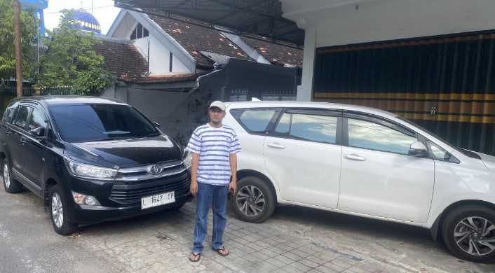 Foto: Koordinator AMSP Nurahmat berdiri di depan dua mobil yang digunakan penyidik Kejati Jatim saat penggeledahan rumah Korkab BSPS Sumenep, Selasa (8/7/2025).